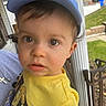 toddler, child, face, cap, yellow_tshirt, dinosaur_print, person, outdoor, porch, column, cross_necklace, brown_eyes, curious_expression, closeup, clothing, daylight, holding, casual, human, young_child