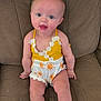 baby, child, infant, couch, clothing, yellow, white, sun_pattern, sitting, smiling, face, legs, arms, cute, indoors, furniture, person, happy, young, portrait