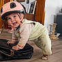 baby_clothes, bag, cat_scratching_post, child, crawling, cute, floor, furniture, happy, helmet, home, indoor, mirror, person, photo_frames, play_mat, smiling, socks, toddler, wooden_floor