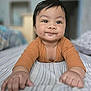 baby, child, infant, smile, face, hands, orange_clothing, bed, striped_bedspread, indoor, person, cute, portrait, lying_down, skin, young_child, closeup, happy, blurred_background, cozy