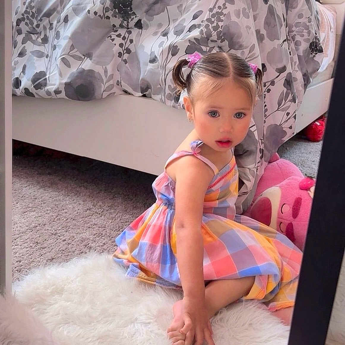 Génesis Martinez is registered to the contest to win money with this photo: bed, bedroom, carpet, casual, child, colorful_dress, curious, furniture, girl, indoor, patterned_bedding, pigtails, pink, plush_toy, rug, sitting, soft_texture, toddler, white, young_child
