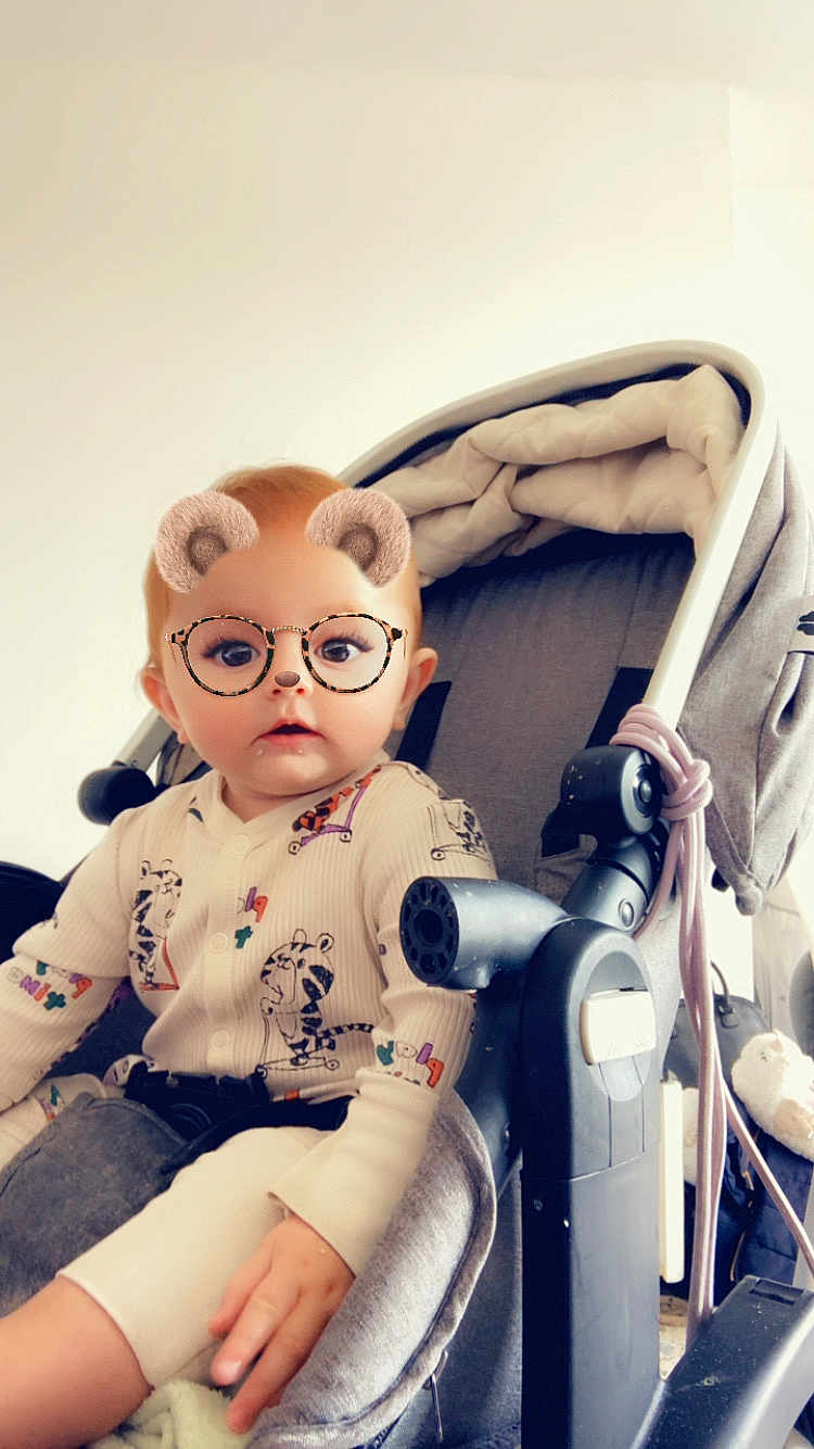 Rose participe au concours pour gagner de l'argent avec cette photo : baby, child, stroller, onesie, patterned_clothing, face_filter, bear_ears, glasses_filter, indoor, infant, cute, seated, hand, expression, light_background, soft_lighting, toy, blanket, person, portrait