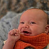 Waylon is registered to the contest to win money with this photo: baby, smiling, infant, orange_bib, face, hand, cozy, blanket, cute, happy, portrait, closeup, skin, child, expression, soft_texture, indoors, newborn, warm_colors, person