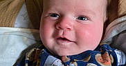 Waylon is registered to the contest to win money with this photo: baby, infant, child, onesie, clothing, smile, face, hand, blanket, indoor, portrait, cute, happy, soft, cozy, closeup, skin, person, expression, newborn