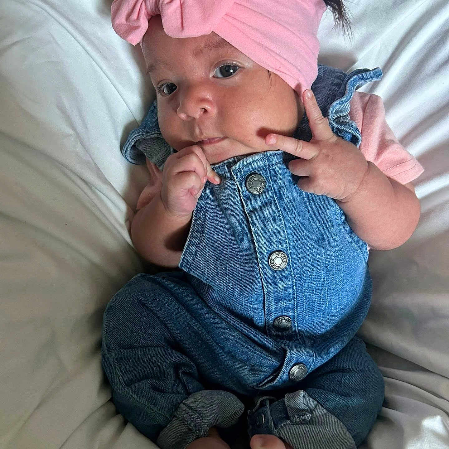 Amelia joined the competition — help win amazing prizes! baby, barefoot, child, chubby_cheeks, clothing, curious, cute, denim_overalls, hand_gesture, headband, indoors, infant, peace_sign, person, pink_bow, portrait, resting, soft, toddler, white_blanket