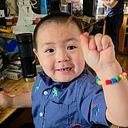 Nicholas is registered to the contest to win money with this photo: child, boy, smiling, bracelet, colorful_beads, blue_shirt, dinosaur_print, kitchen, appliance, mixer, cup, adult, woman, glasses, cabinet, counter, chair, happy, indoor, person