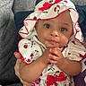 baby, bonnet, cherry_pattern, child, closeup, clothing, couch, cozy, curious, cute, face, hand_holding, hands, indoor, infant, person, portrait, red_bow, smile, soft_lighting