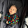 baby, child, stroller, colorful_sweater, blue_eyes, curly_hair, seatbelt, gray_fabric, infant, outdoor, portrait, cute, casual_clothing, comfort, person, young_child, bright_colors, knitted_sweater, looking_up, seated