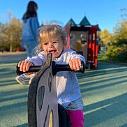 Maïween a rejoint le concours — aidez-le/la à gagner de superbes lots ! toddler, child, playground, play_equipment, ride, happy, smiling, outdoor, daylight, blue_sky, person, toy, fun, girl, handlebar, casual_clothing, shadow, park, play, cute