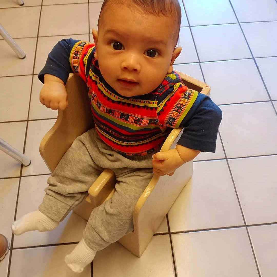 Léo participe au concours pour gagner de l'argent avec cette photo : baby, casual_wear, chair, child, colorful_clothing, curious, cute, floor_tiles, gray_pants, indoor, infant, looking_up, patterned_shirt, seated, small_hands, tiled_floor, toddler, white_socks, wooden_chair, young_child