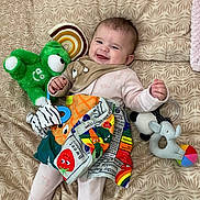 Eliora joined the competition — help win amazing prizes! baby, smiling, toy, stuffed_animal, blanket, colorful, pattern, happy, infant, lying_down, clothing, cute, playful, child, fabric, soft_toy, indoors, face, head, hand