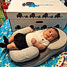 baby, baby_bundle_box, bedspread, black_shorts, blue_bedspread, child, clothing, colorful, comfortable, cushion, cute, elephant_logo, face, home, indoor, infant, lying_down, patterned_bedspread, person, white_shirt