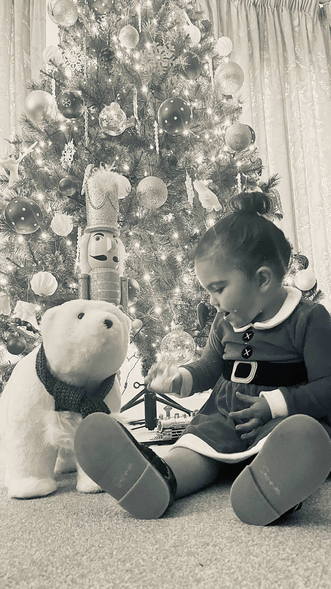 Ava Mae is registered to the contest to win money with this photo: black, black_and_white, christmas_decoration, christmas_ornament, christmas_tree, event, facial_expression, happy, holiday_ornament, human_body, monochrome, monochrome_photography, ornament, people, person, photograph, snapshot, standing, toddler, toy