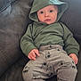 baby, child, hoodie, green_clothing, gray_pants, fire_truck_pattern, couch, furniture, indoors, wide_eyes, expression, person, infant, casual_clothing, relaxing, seated, comfortable, soft_fabric, home, cute