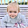 toddler, child, smiling, bench, outdoor, fleece_jacket, pink_shoes, wooden_bench, happy, face, person, cute, playful, park, daylight, hair_tie, casual_clothing, young_child, nature, portrait
