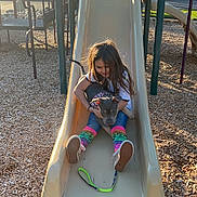 Myka Blu is registered to the contest to win money with this photo: child, dog, slide, playground, wood_chips, outdoor, daylight, happy, casual_clothing, jeans, colorful_socks, puppy, bandana, playing, fun, smiling, leash, park, tree, plastic_slide