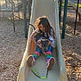 child, dog, slide, playground, wood_chips, outdoor, daylight, happy, casual_clothing, jeans, colorful_socks, puppy, bandana, playing, fun, smiling, leash, park, tree, plastic_slide