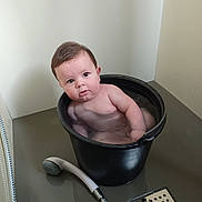 Marceau a rejoint le concours — aidez-le/la à gagner de superbes lots ! baby, bucket, water, bathroom, showerhead, floor, wall, child, naked, face, expression, plumbing, indoor, curious, black_bucket, wet, person, skin, head, tub