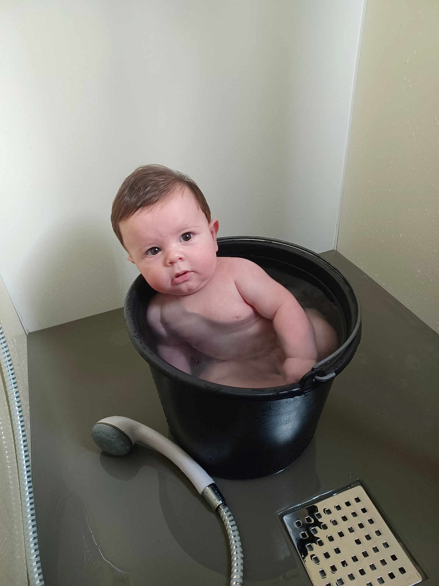 Marceau a rejoint le concours — aidez-le/la à gagner de superbes lots ! baby, bucket, water, bathroom, showerhead, floor, wall, child, naked, face, expression, plumbing, indoor, curious, black_bucket, wet, person, skin, head, tub