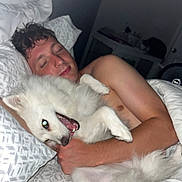 Novah joined the competition — help win amazing prizes! person, dog, bed, pillow, blanket, cuddling, sleeping, happy, indoor, night, closeup, white_dog, fluffy, smiling, relaxed, human, pet, comfort, resting, cozy
