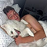 person, dog, bed, pillow, blanket, cuddling, sleeping, happy, indoor, night, closeup, white_dog, fluffy, smiling, relaxed, human, pet, comfort, resting, cozy