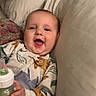 baby, child, infant, smiling, happy, portrait, face, sitting, lying_down, bed, pillow, blanket, bottle, feeding, onesie, clothing, indoor, bedroom, cozy, baby_toy