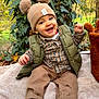 baby, blanket, child, cozy, fall, greenery, happy, hat, leaves, nature, outdoor, pants, plaid_shirt, pom_poms, shoes, sitting, smile, toy, tree_trunk, vest