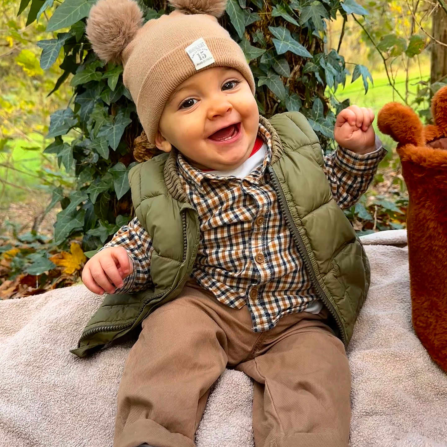 Sowen participe au concours pour gagner de l'argent avec cette photo : baby, blanket, child, cute, fall, greenery, happy, hat, ivy, nature, outdoor, pants, plaid_shirt, pom_pom, portrait, sitting, smiling, sneakers, tree, vest