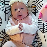 Bailey Lee is registered to the contest to win money with this photo: baby, infant, headband, flower, pink_clothing, white_sleeves, patterned_cushion, leaf_pattern, indoor, person, cute, young_child, portrait, seated, soft_toys, child, expression, closeup, comfort, fabric