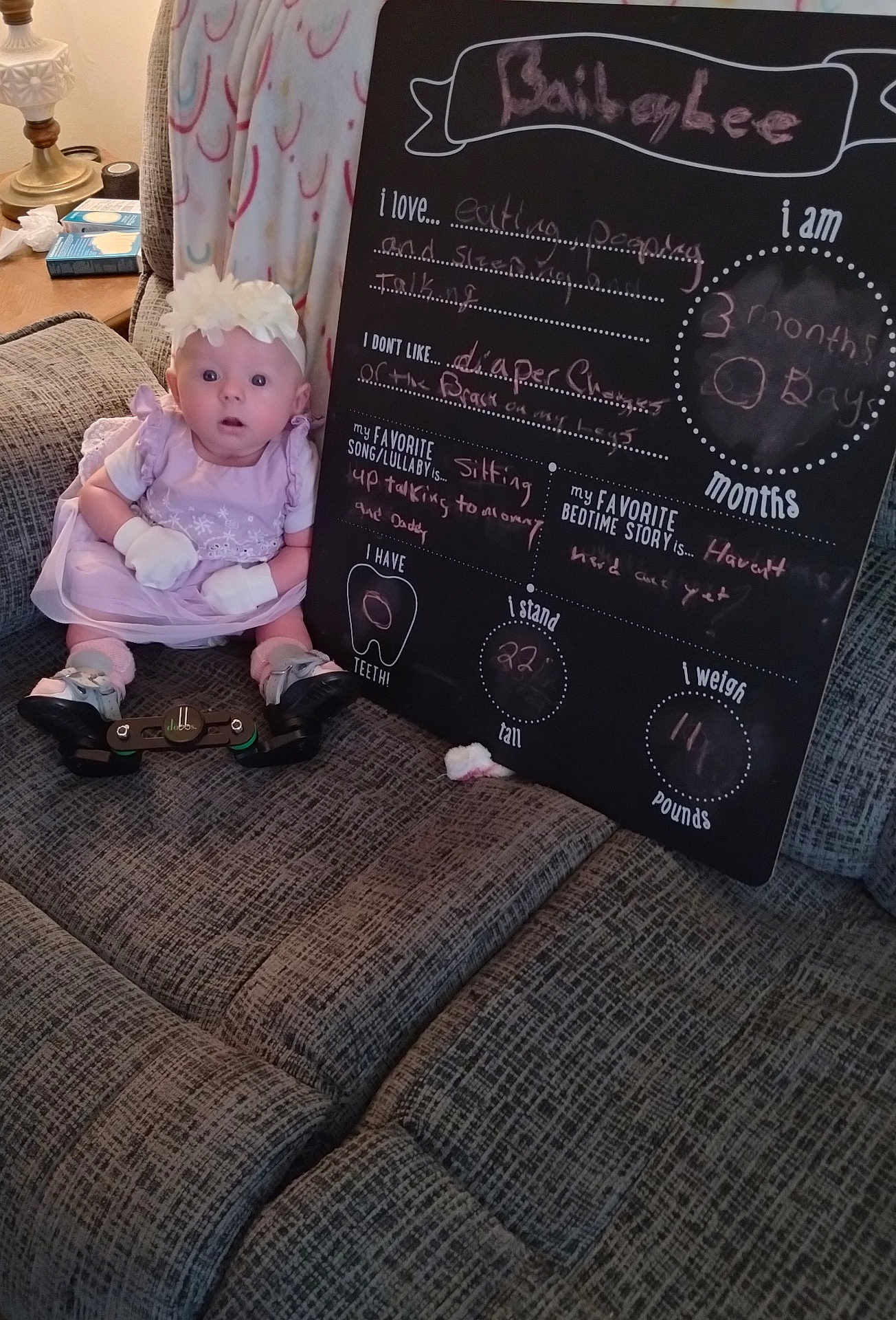 Bailey Lee joined the competition — help win amazing prizes! baby, infant, dress, gloves, headband, couch, blanket, blackboard, writing, milestones, living_room, lamp, furniture, person, sitting, cute, expression, indoor, child, young