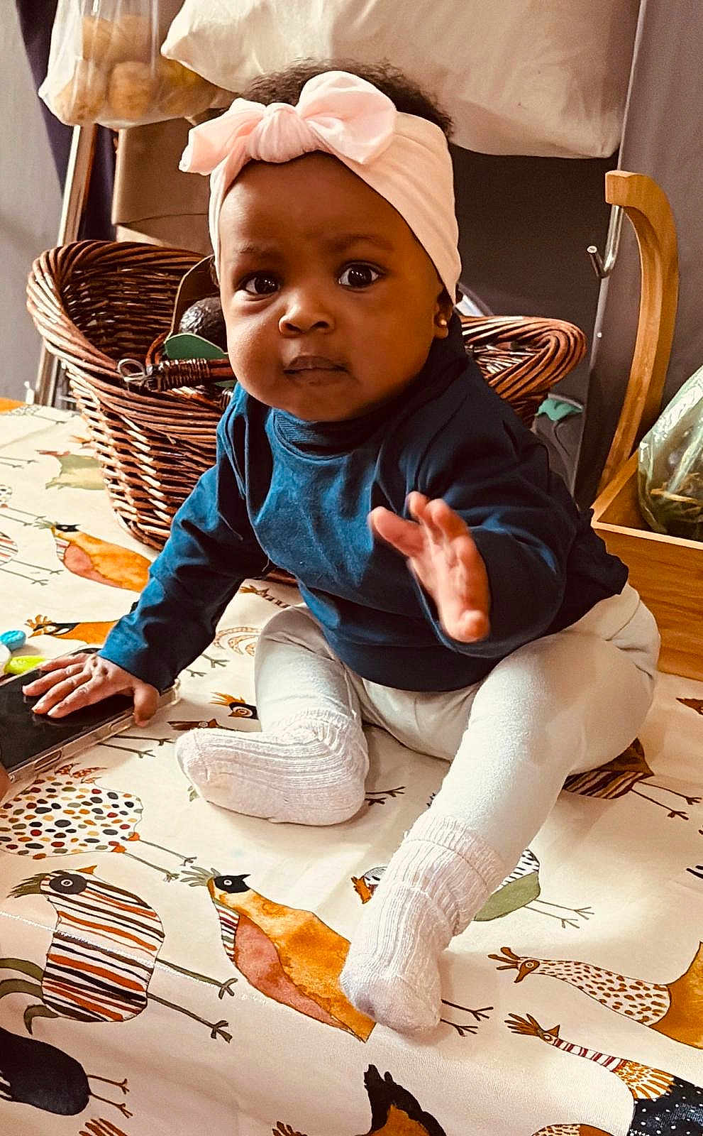 Isabelle joined the competition — help win amazing prizes! baby, child, headband, socks, blue_shirt, blanket, bird_pattern, basket, indoor, curious, sitting, hand, face, cozy, home, decor, wooden_chair, table, toy, infant