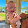 baby, smiling, child, person, holding, arm, skin, face, indoors, window, daylight, blurred_background, happiness, joy, cute, infant, apparel, sleeveless, closeup, portrait