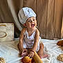 baby, child, chef_hat, apron, bread, pastries, rolling_pin, smile, happy, sitting, food, baking, kitchen, white_cloth, cute, infant, portrait, indoors, playful, cooking