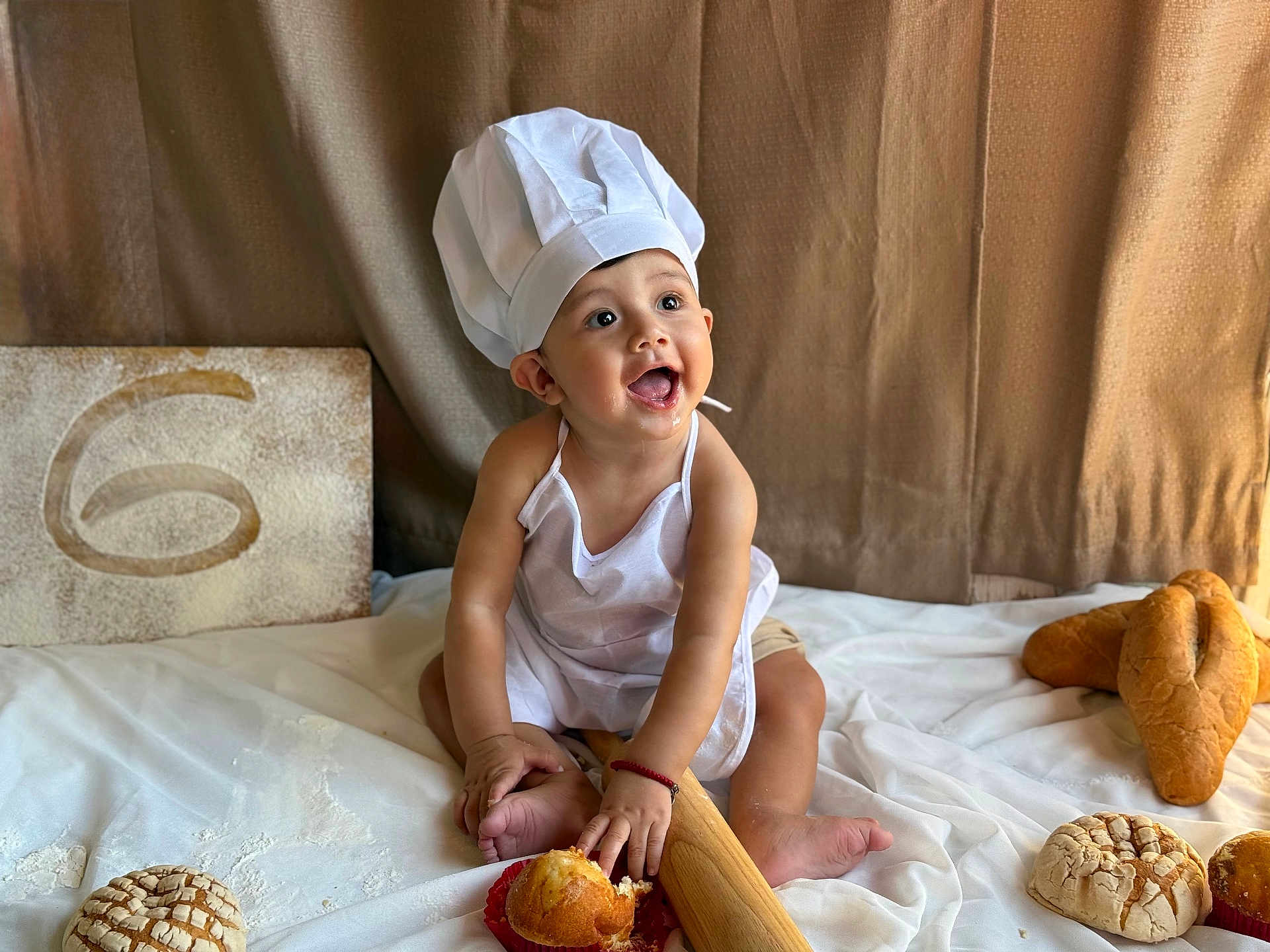 Luis Adriel is registered to the contest to win money with this photo: baby, child, chef_hat, apron, bread, pastries, rolling_pin, smile, happy, sitting, food, baking, kitchen, white_cloth, cute, infant, portrait, indoors, playful, cooking
