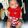 baby, infant, child, car_seat, red_clothing, striped_shorts, american_flag, patriotic, expression, serious_face, indoor, blanket, warning_label, footwear, person, sitting, portrait, cute, holiday, celebration