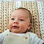 baby, infant, face, blue_eyes, knit_blanket, overalls, white_shirt, skin, head, cheeks, portrait, cute, child, newborn, lying_down, soft_texture, warm_colors, indoors, smiling, happy