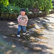 Carson joined the competition — help win amazing prizes! toddler, child, boy, cap, tshirt, jeans, shoes, puddle, water, outdoor, sunlight, shadow, pathway, greenery, plants, stone_wall, happy, walking, nature, play