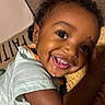 Purpose joined the competition — help win amazing prizes! child, toddler, smiling, happy, portrait, face, close_up, curly_hair, brown_skin, teeth, eyes, white_shirt, bed, blanket, indoor, home, cozy, candid, adult_arm, photography