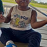 Purpose is registered to the contest to win money with this photo: child, toddler, portrait, sitting, outdoor, porch, deck, wooden_floor, sunny, smiling, face, short_hair, dark_skin, sleeveless_shirt, graphic_shirt, pants, colorful_socks, snack, food_on_face, road