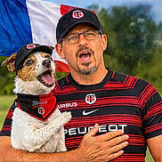 Stuarts a rejoint le concours — aidez-le/la à gagner de superbes lots ! dog, man, person, outdoor, portrait, french_flag, sports_jersey, matching_outfits, baseball_cap, glasses, mustache, beard, open_mouth, barking, happy, pet, holding_dog, sponsor_logo, greenery, patriotic