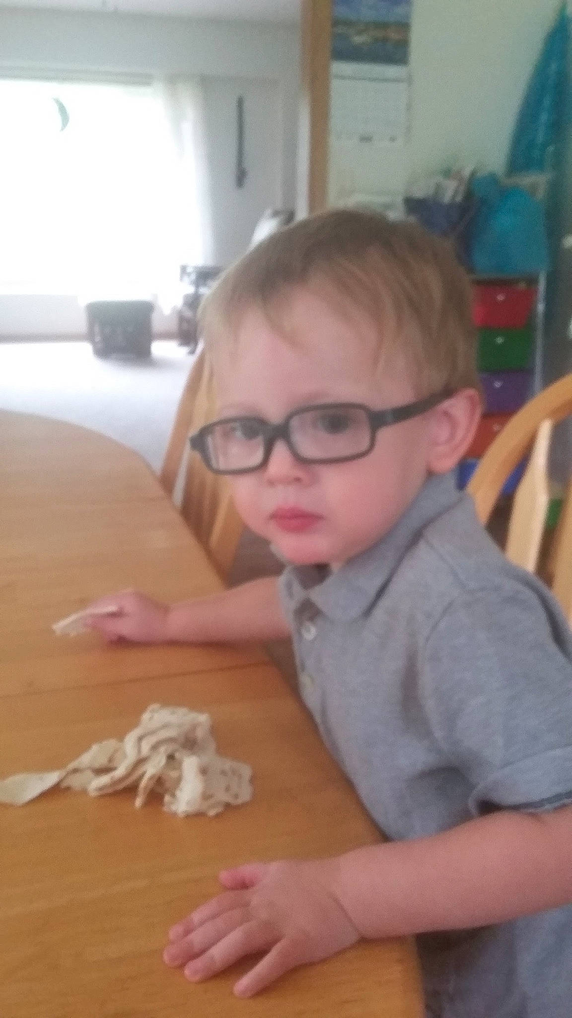 Caleb is registered to the contest to win money with this photo: chair, child, eyewear, face, floor, flooring, fun, glasses, hardwood, person, plywood, room, sitting, table, thumb, toddler, varnish, vision_care, wood, wood_flooring