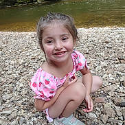 Natalie is registered to the contest to win money with this photo: child, girl, smiling, outdoor, river, rocks, picnic, food, snacks, sneakers, dress, pink, nature, happy, crouching, daylight, hair, face, person, playful