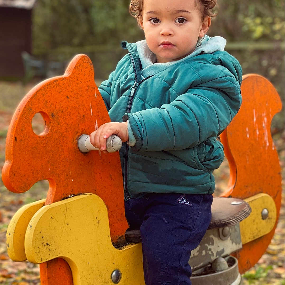 Ely participe au concours pour gagner de l'argent avec cette photo : child, toddler, playground, spring_ride, orange, yellow, jacket, boots, autumn, leaves, outdoor, nature, park, toy, curly_hair, casual_clothing, daytime, play, person, forest