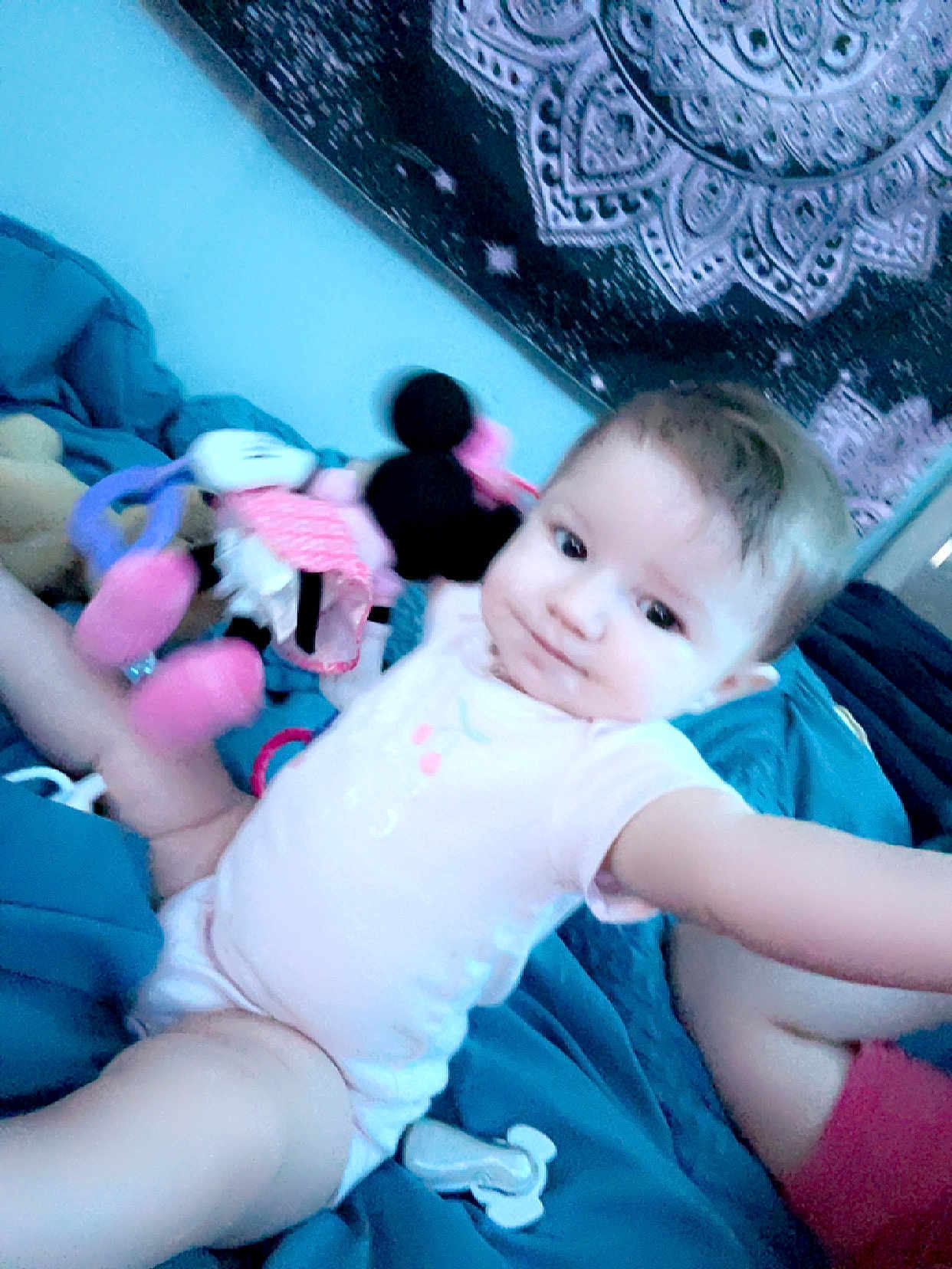 Amelia is registered to the contest to win money with this photo: baby, child, infant, onesie, toy, plush, minnie_mouse, bed, blanket, blue, tapestry, pattern, indoor, person, face, smile, legs, arm, room, cute