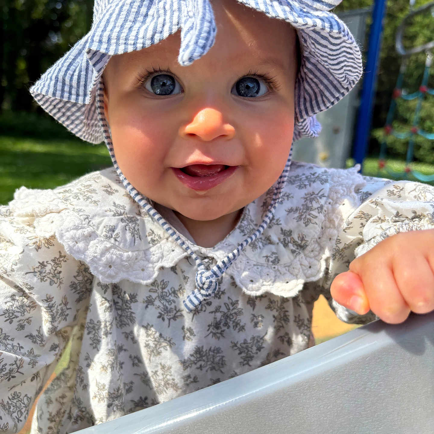 Thaïs a rejoint le concours — aidez-le/la à gagner de superbes lots ! baby, blue_sky, child, cute, daylight, dress, face, grass, hand, happy, hat, infant, outdoor, person, playground, slide, smiling, sun_hat, sunlight, trees