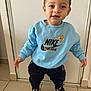 Bastien participe au concours pour gagner de l'argent avec cette photo : child, toddler, standing, smiling, portrait, blue_sweatshirt, nike_logo, sneakers, shoes, tile_floor, indoor, door, brown_hair, eyes, hands, casual_clothing, cute, happy, frontal_pose, background_wall