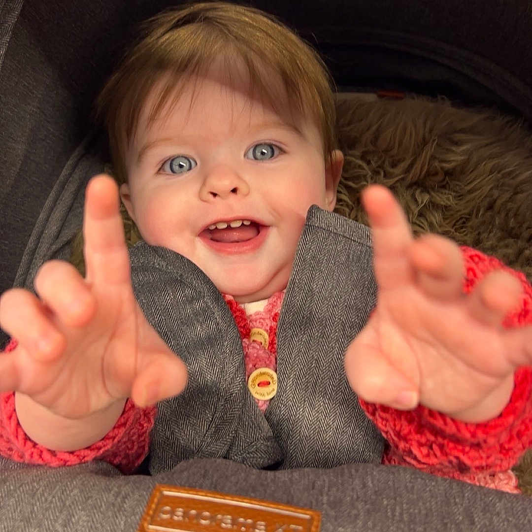 Thea joined the competition — help win amazing prizes! baby, bodypart, clothing, coat, cushion, face, finger, furniture, hand, happy, head, homedecor, jacket, laughing, pants, person, photography, portrait, smile, text