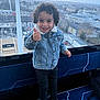 Gonçalves participe au concours pour gagner de l'argent avec cette photo : child, curly_hair, thumbs_up, denim_jacket, black_pants, white_sneakers, indoor, window, cityscape, cable_car, gondola, smiling, standing, urban, daylight, transportation, blue_seat, happy, person, young