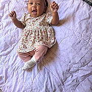 Blakely joined the competition — help win amazing prizes! baby, child, infant, smiling, happy, lying_down, blanket, quilt, floral_dress, pink_leggings, headband, indoors, cute, raised_hands, expressive_face, soft_lighting, fabric, pattern, person, toddler