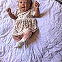 baby, child, infant, smiling, happy, lying_down, blanket, quilt, floral_dress, pink_leggings, headband, indoors, cute, raised_hands, expressive_face, soft_lighting, fabric, pattern, person, toddler